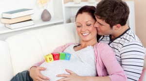 young man kissing his pregnant wife with baby letters on the belly lying on the sofa